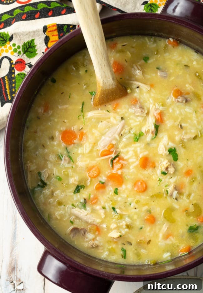 Velvety Chicken and Rice Soup 2 A whole pot of creamy chicken and rice soup with a wooden spoon, ready to serve.