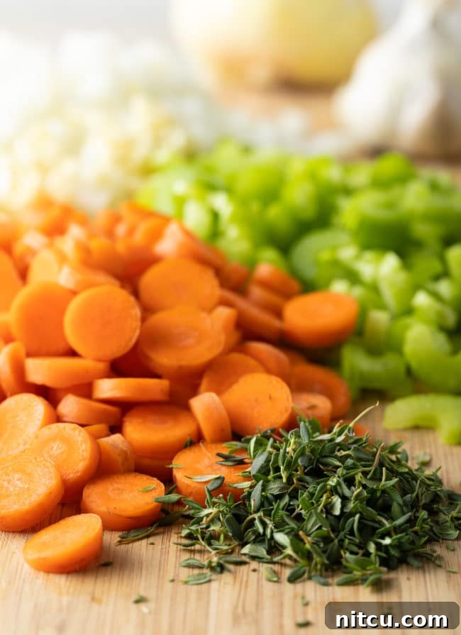 Velvety Chicken and Rice Soup 4 Assortment of freshly chopped vegetables, including onions, carrots, and celery, on a wooden cutting board.