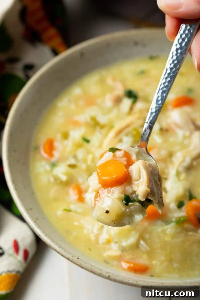 Velvety Chicken and Rice Soup 8 A hand holding a spoon with a spoonful of creamy chicken and rice soup, lifted above a full bowl.