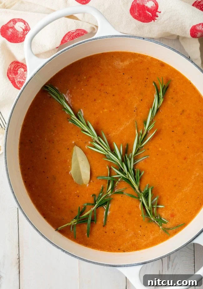 Velvety Roasted Tomato and Basil Soup 2 Overhead shot of creamy roasted tomato soup in a large Dutch oven garnished with fresh basil sprigs.