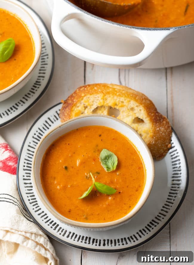 Velvety Roasted Tomato and Basil Soup 12 Two cozy bowls of creamy roasted tomato soup with a large pot of more soup in the blurred background, inviting warmth.