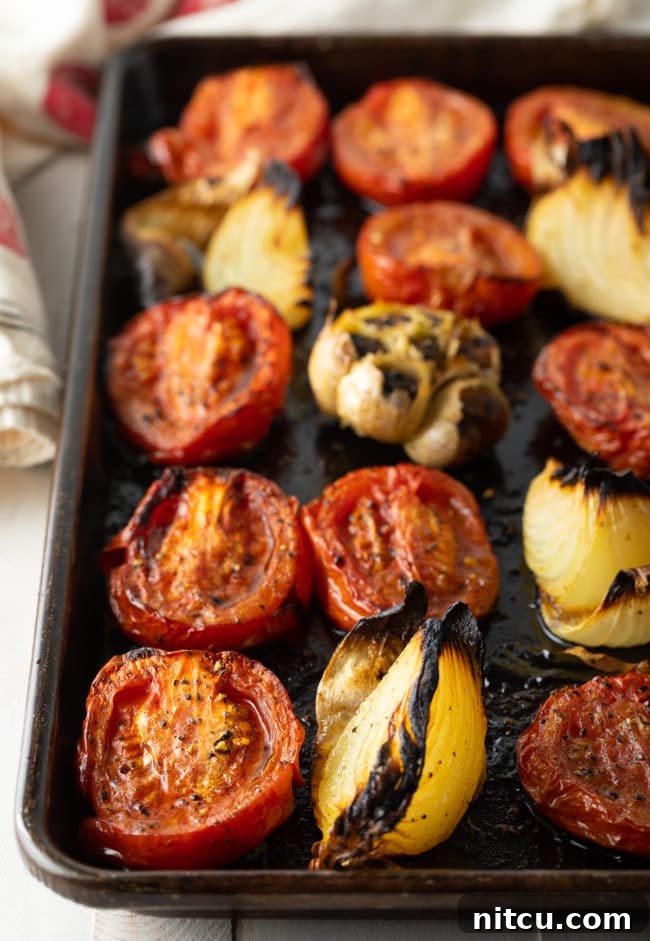 Velvety Roasted Tomato and Basil Soup 6 Roasted tomatoes, softened garlic cloves, and caramelized onion wedges on a baking sheet after being removed from the oven.