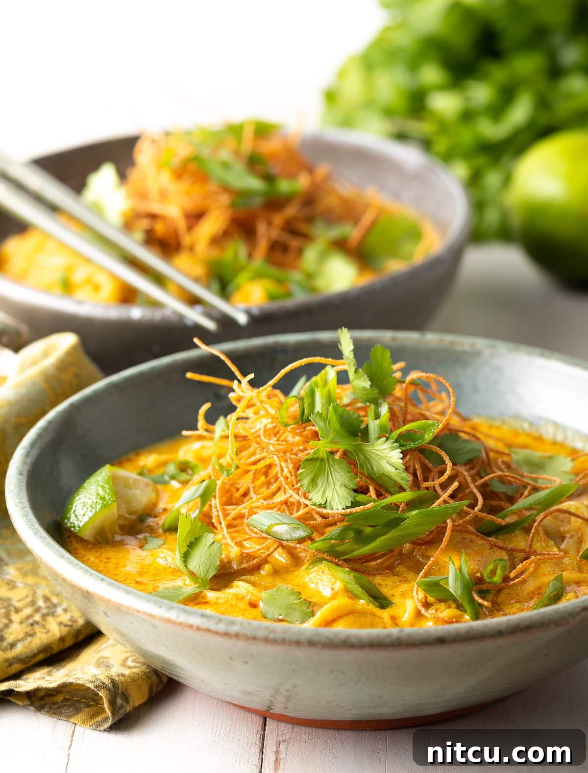 A side view of a steaming bowl of coconut curry soup, showcasing the vibrant colors of the broth and garnishes.