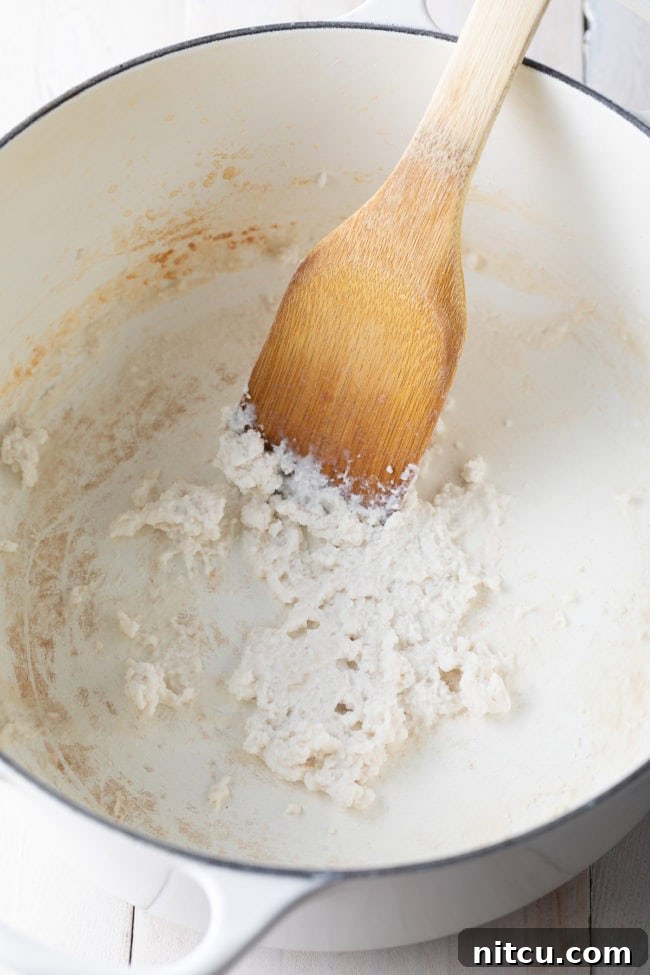 Unsweetened coconut milk reducing in a pot, becoming a thick, flavorful paste for the Khao Soi broth.