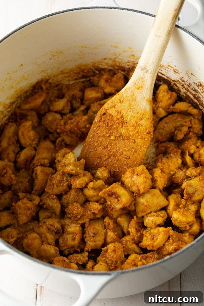 Diced chicken pieces simmering in the rich, vibrant red curry and coconut milk broth for Khao Soi.