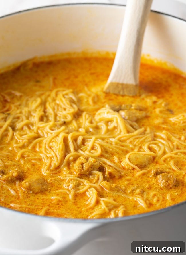 The Khao Soi broth, rich and creamy, simmering gently with tender chicken pieces, developing its deep flavors.