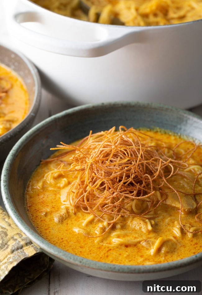 A close-up of a bowl of Khao Soi, beautifully topped with golden fried noodles, fresh cilantro, and a lime wedge, ready to be enjoyed.