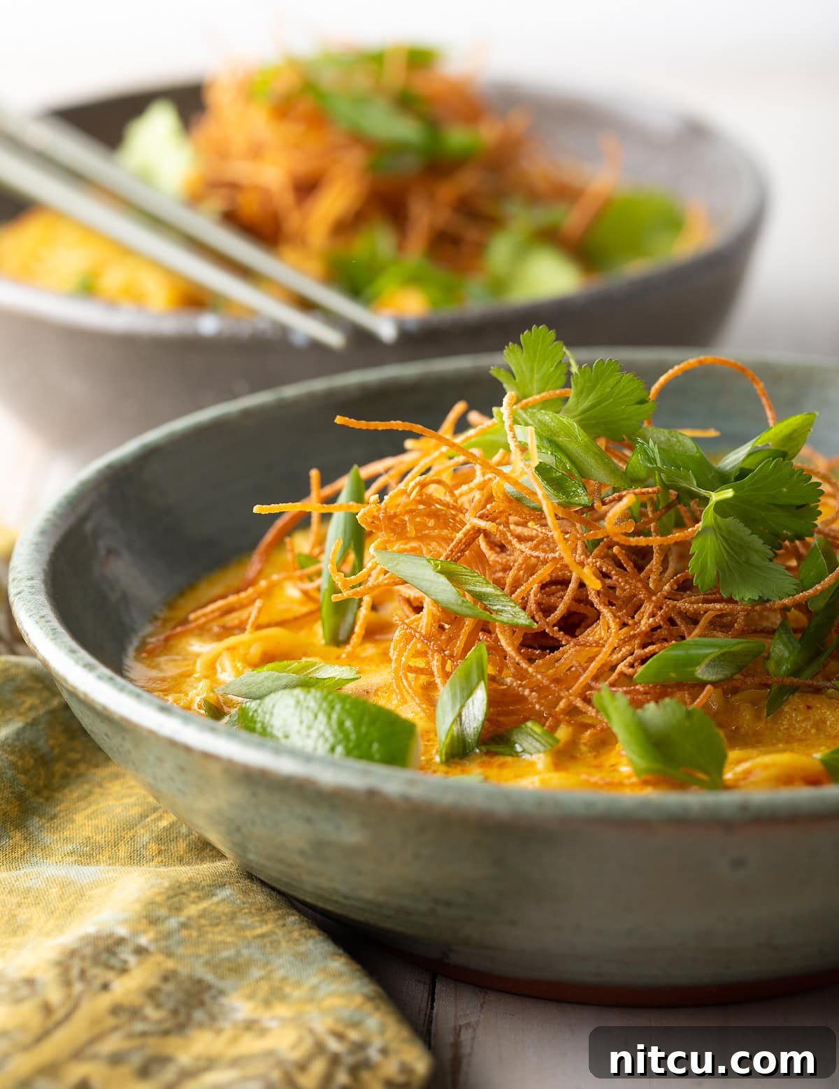 A side view of two gray bowls of rich, flavorful coconut curry soup, garnished and ready to be served.