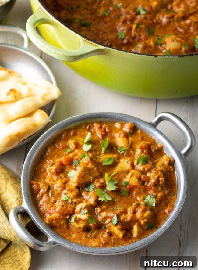 Fiery Madras Chicken 11 Easy Chicken Madras Curry in a silver bowl next to naan bread and a dutch oven.