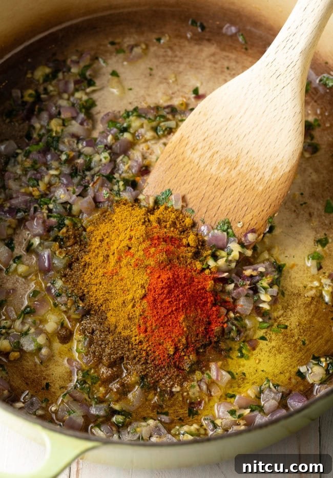 Fiery Madras Chicken 6 Spices and aromatics in a dutch oven being sautéed and stirred with a wooden spoon.