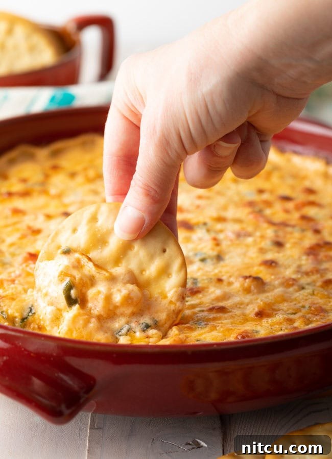 Fiery Cajun Shrimp Dip 12 Hand scooping out hot shrimp dip with a cracker.