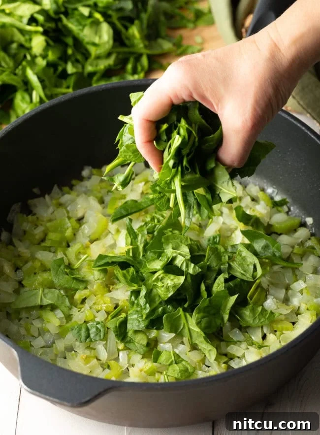 Savory Spinach Pie 4 A large pot filled with sautéed onions, celery, and chopped fresh spinach, slowly wilting down to create the flavorful base for the pie filling.