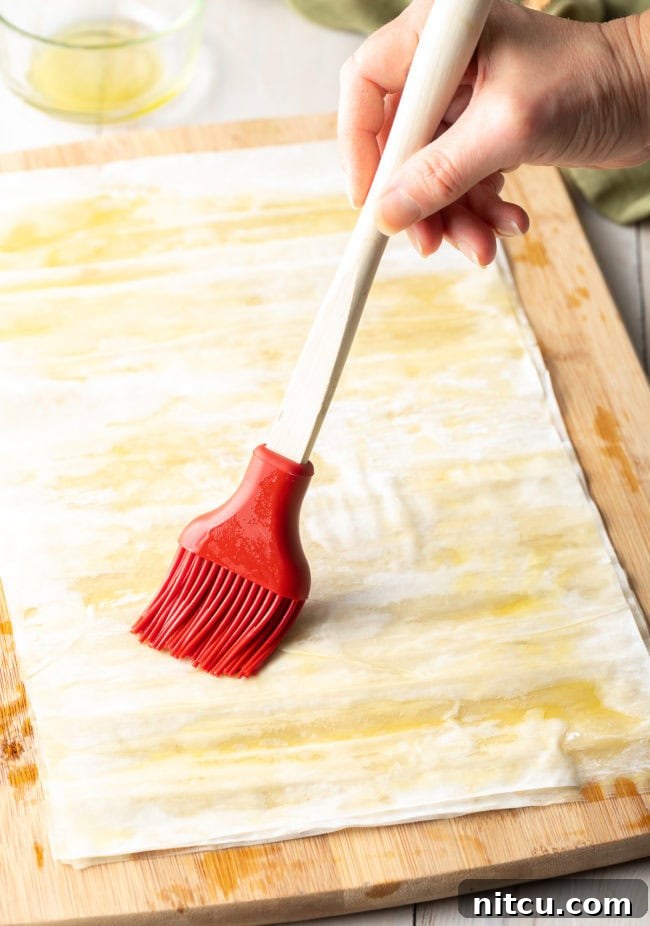 Savory Spinach Pie 9 A hand expertly brushing a thin, even layer of melted ghee onto a single sheet of delicate phyllo dough, preparing it for layering.