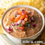 A bowl of fresh homemade bean dip, topped with pico de gallo, ready to be served.