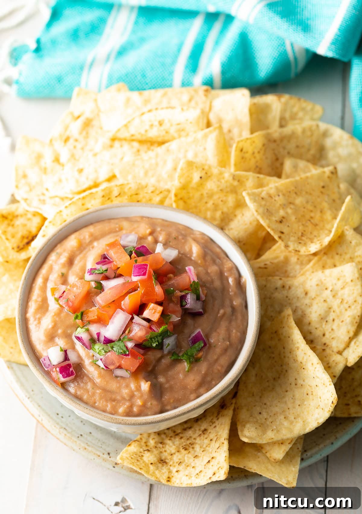Ultimate Homemade Bean Dip 4 A bowl of rich pinto bean dip, topped with vibrant pico de gallo, served alongside a platter of crunchy tortilla chips, ready for snacking.