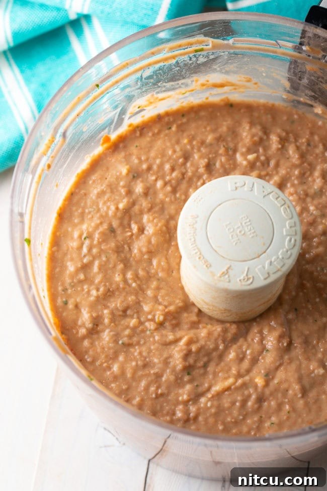 Ultimate Homemade Bean Dip 9 Freshly blended bean dip being spooned into a serving bowl, ready for garnishing.