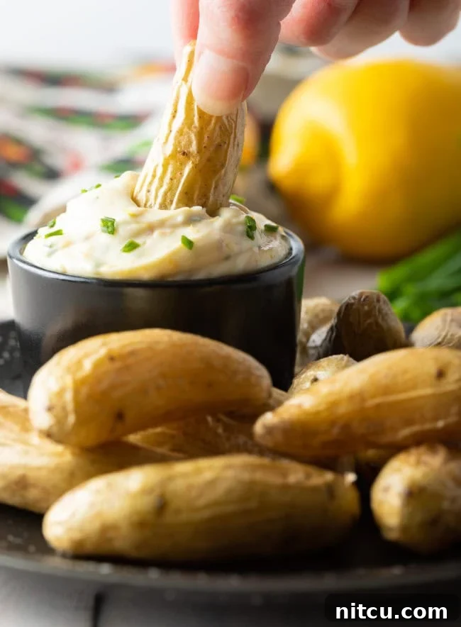 Enchanted Aioli 3 A hand dipping a fingerling potato into a bowl of aioli sauce on a plate with fingerlings.