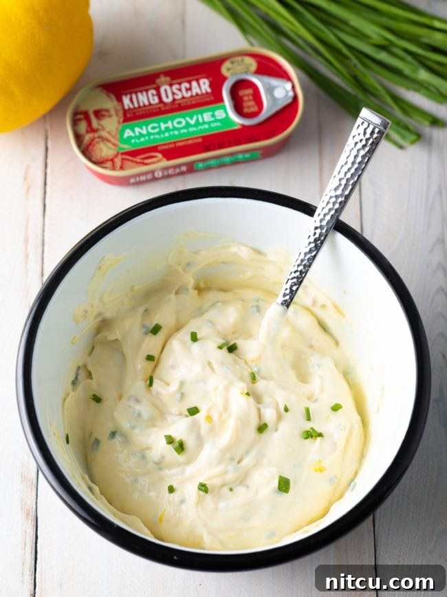 Enchanted Aioli 6 A white bowl with ingredients for aioli sauce with a spoon that has stirred the mixture.
