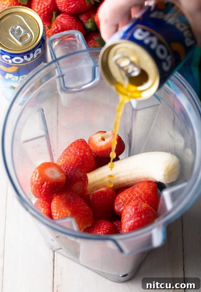 Smoothie King Caribbean Way: Your Tropical Getaway Recipe 5 Strawberries and banana in a blender with papaya nectar being poured in.