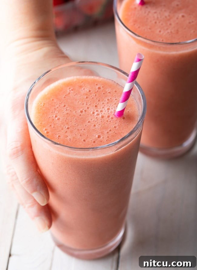 Smoothie King Caribbean Way: Your Tropical Getaway Recipe 8 Hand holding a strawberry banana smoothie with a straw in it.