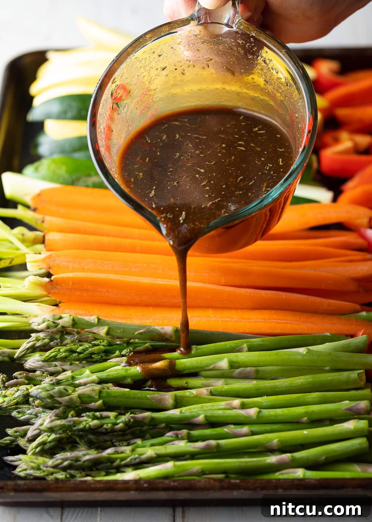 Perfect Grilled Vegetable Marinade 7 Pouring the homemade marinade over raw, cut vegetables on a baking sheet, ready for grilling.