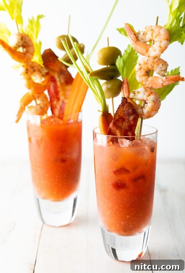 Your Signature Bloody Mary Base 5 Closeup view of 2 Bloody Mary cocktails garnished with shrimp, bacon, celery, olives and carrots.