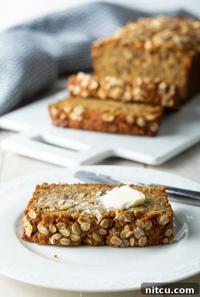 Wholesome Oat & Banana Loaf 13 A delectable slice of banana bread on a plate, elegantly topped with a delicate smear of melted butter.