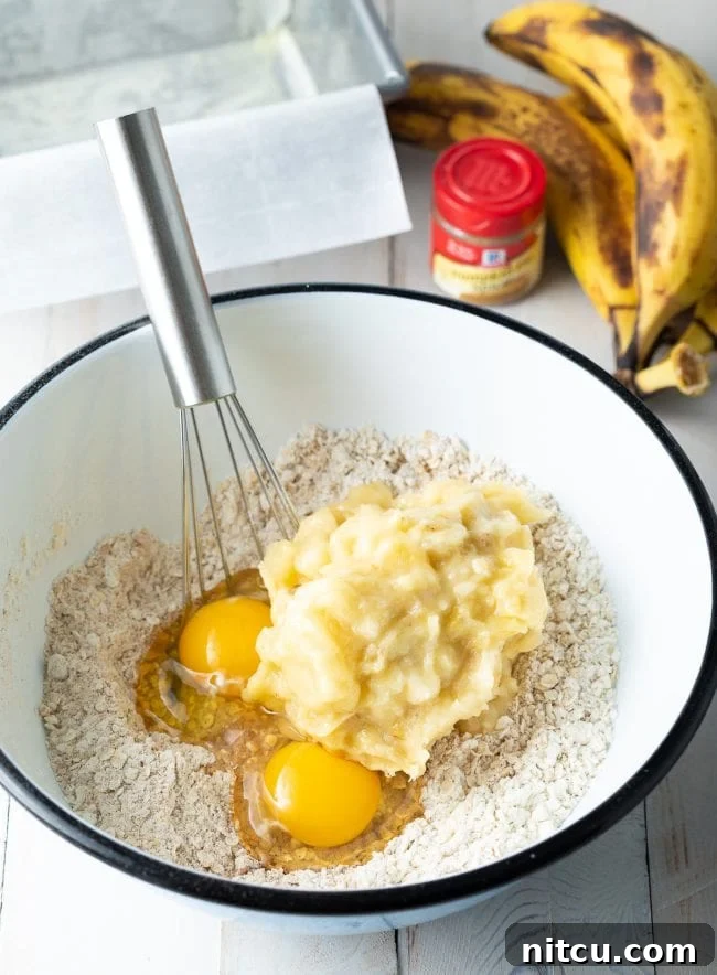 Wholesome Oat & Banana Loaf 7 Flour and oats with mashed banana and eggs in a mixing bowl.