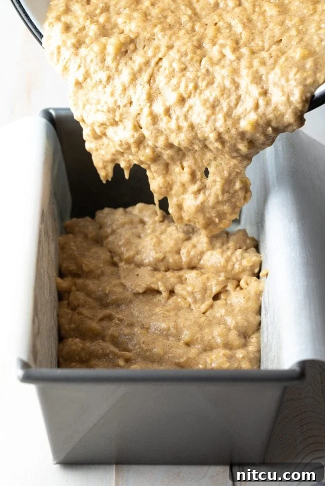 Wholesome Oat & Banana Loaf 9 Banana bread batter being transferred into a baking dish lined with parchment paper for easy removal.