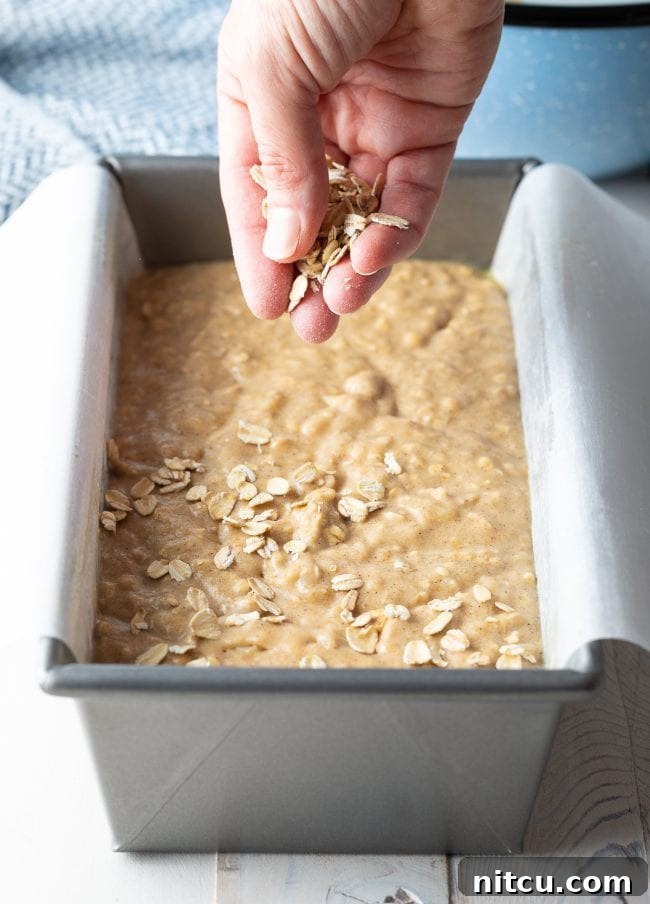 Wholesome Oat & Banana Loaf 10 A hand gently sprinkling extra oats onto the top of banana bread batter before baking.