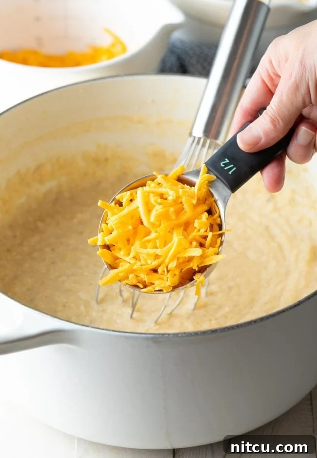 Golden Cheesy Comfort 5 Grits in a stockpot with cheddar cheese being stirred in.
