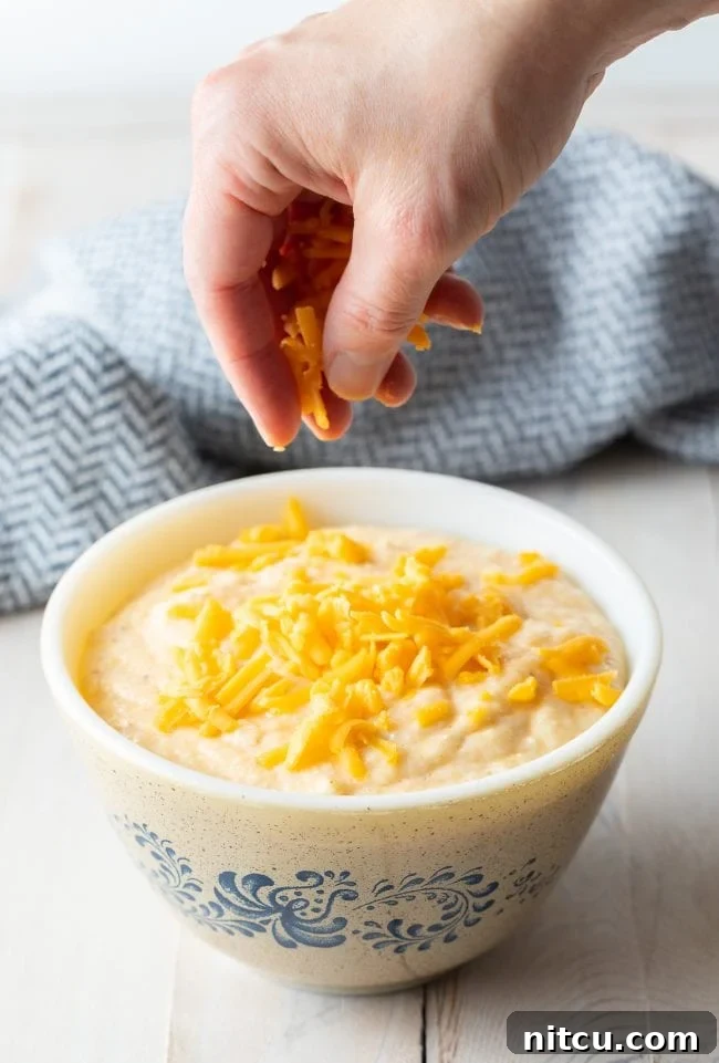 Golden Cheesy Comfort 7 Bowl of grits with a hand above it sprinkling cheese on top.