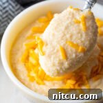A bowl of creamy cheese grits with a small serving spoon.