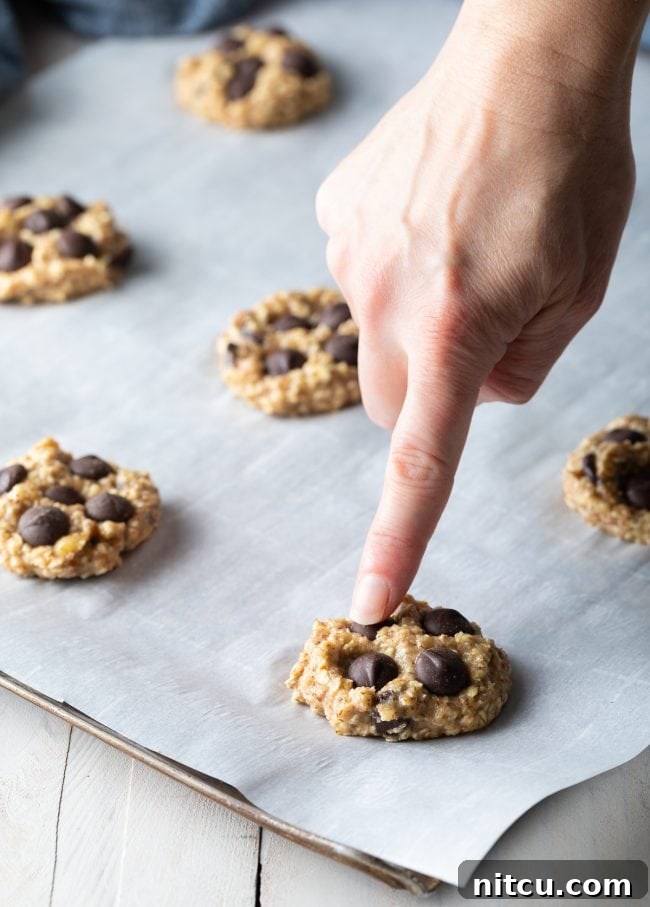 Banana Bread Bliss Chocolate Chip Cookies 8 Hand pointing to a chocolate chip in a banana oat cookie on parchment paper.