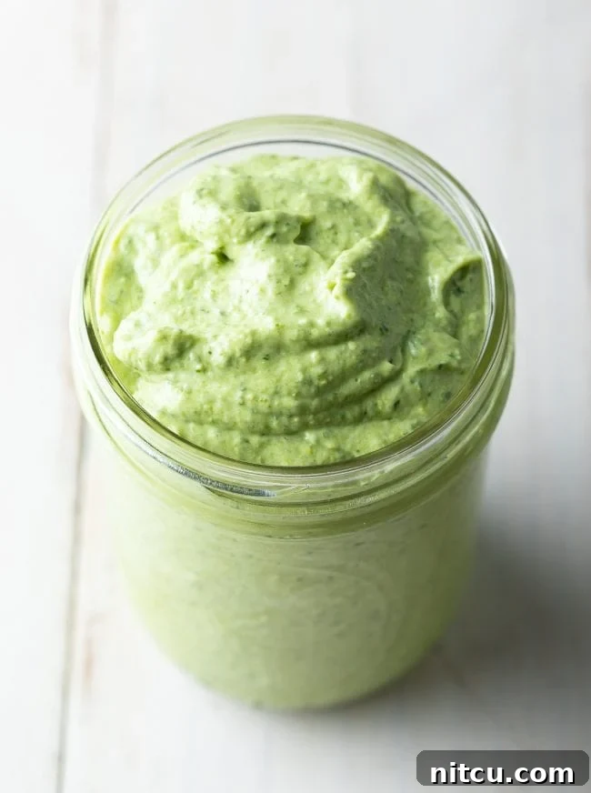 Velvety Pesto Perfection 2 A close-up shot of a jar filled with luscious, vibrant green creamy pesto sauce, ready to be enjoyed.