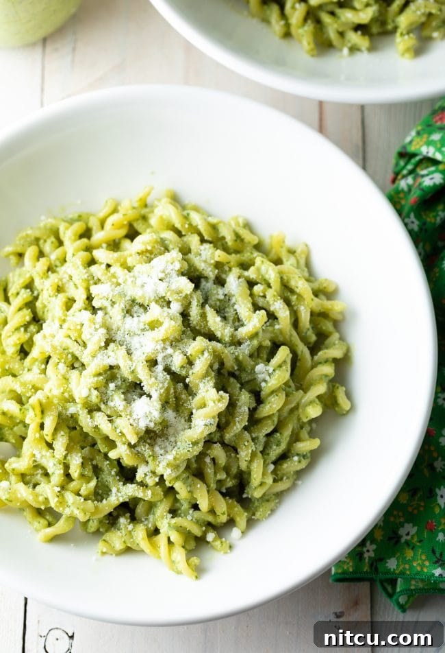 Velvety Pesto Perfection 5 Delicious fusilli pasta generously coated in creamy pesto sauce, garnished with grated Parmesan cheese, served in an elegant white bowl.