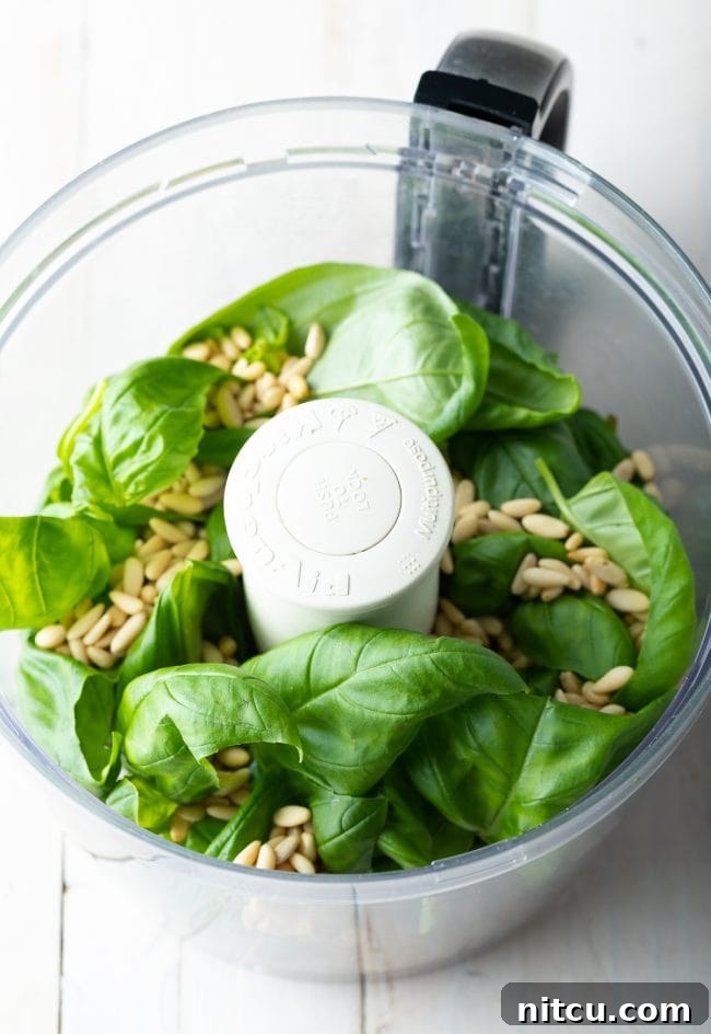 Velvety Pesto Perfection 6 Fresh basil leaves and pine nuts placed inside a food processor, ready for blending.