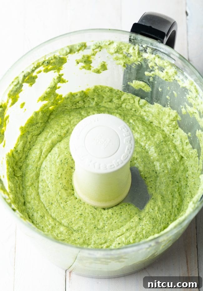 Velvety Pesto Perfection 7 Smooth, vibrant green creamy pesto sauce in a food processor bowl after being thoroughly mixed.