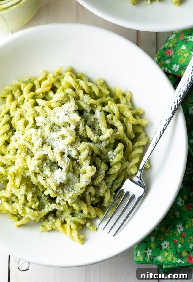 Velvety Pesto Perfection 10 An inviting overhead view of pesto pasta in a white bowl, adorned with fresh basil, accompanied by a fork resting beside it.