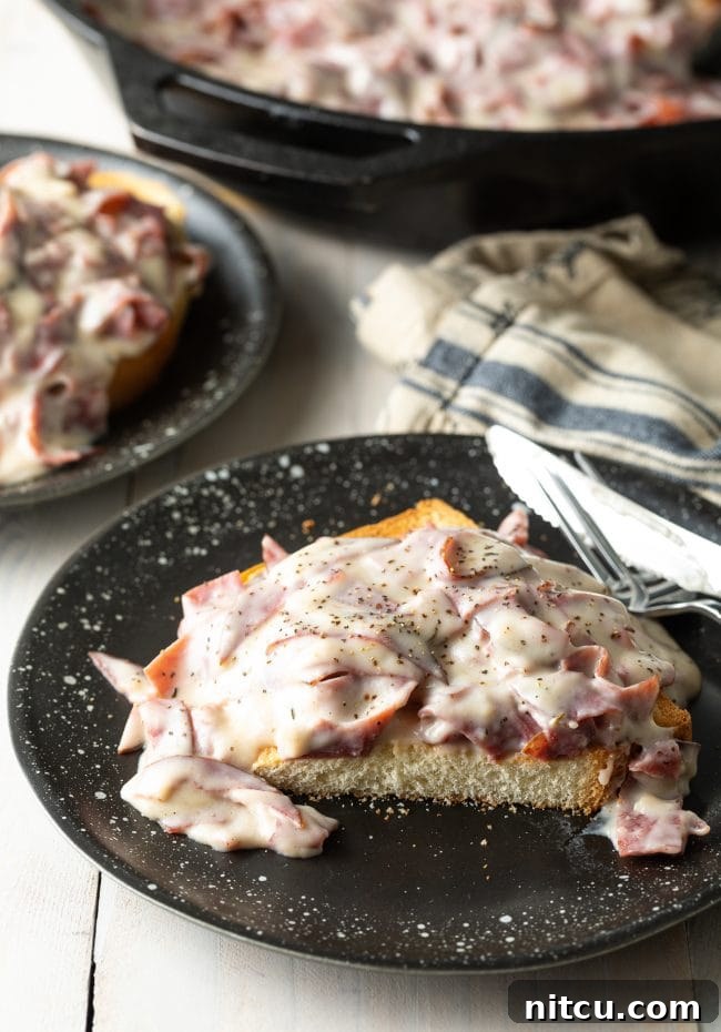 Classic Creamed Beef Toast 4 Creamed chipped beef on top of toast, cut in half, showcasing its rich texture on a black plate.