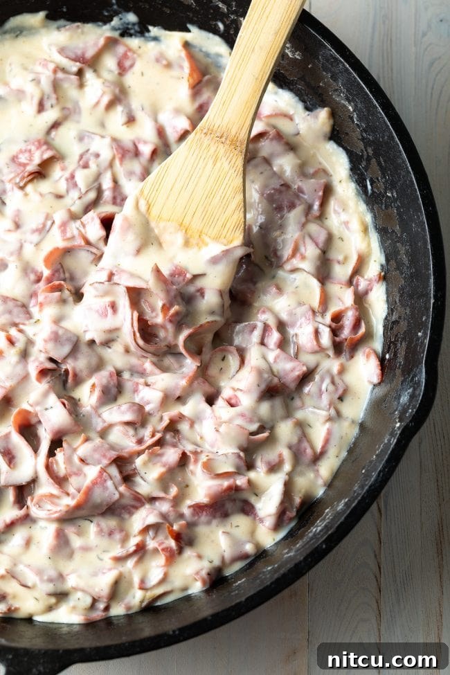 Classic Creamed Beef Toast 6 Rich, homemade chipped beef gravy simmering in a cast iron skillet, stirred with a wooden spoon.