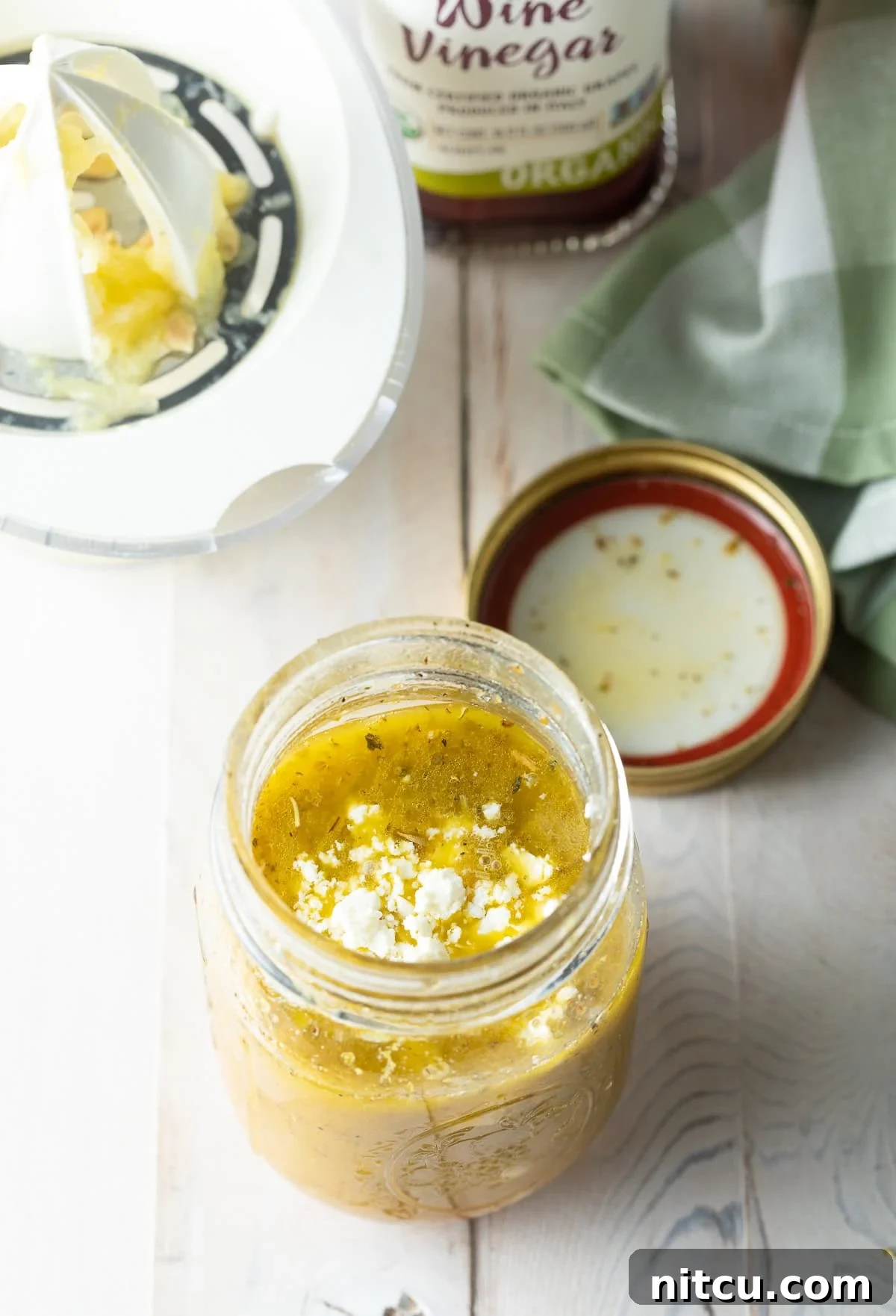 Zesty Greek Vinaigrette 7 A close-up of a hand pouring red wine vinegar into a jar, a key ingredient for tang.