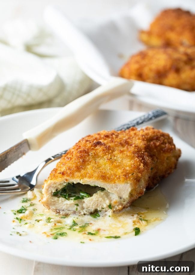 Effortless Golden Chicken Kiev 2 Golden brown pan-fried Chicken Kiev, expertly cut open to reveal its luscious, melting garlic butter filling, elegantly served on a plate with a fork poised for a bite.