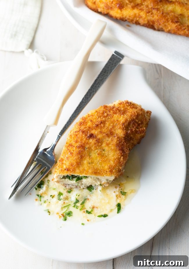 Effortless Golden Chicken Kiev 11 A mesmerizing close-up of a pan-fried Chicken Kiev, elegantly sliced open to prominently display the luscious, melted garlic butter gently oozing out onto a pristine white plate, promising an exquisite culinary experience.
