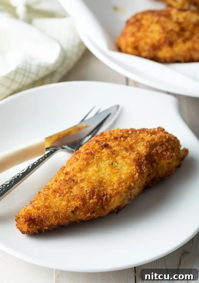 Effortless Golden Chicken Kiev 12 A perfectly cooked, simplified pan-fried Chicken Kiev presented with a fork and knife on a crisp white plate, elegantly showcasing its golden crust and inviting texture, ready to be savored.