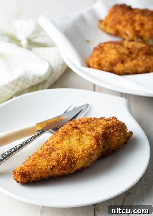 Effortless Golden Chicken Kiev 4 A perfectly golden-brown, crispy pan-fried Chicken Kiev served elegantly on a pristine white plate, accompanied by a fork, highlighting its exquisite texture and readiness to be savored.