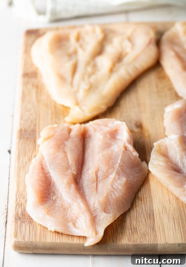 Effortless Golden Chicken Kiev 5 Raw chicken breasts, precisely butterflied and laid flat on a rustic wooden cutting board, meticulously prepared and ready for the stuffing process.