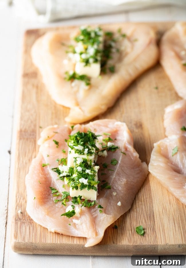 Effortless Golden Chicken Kiev 6 Butterflied chicken breasts with carefully placed mounds of creamy, herb-infused garlic butter filling situated in the center on a wooden cutting board.