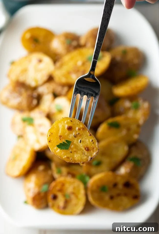 Zesty Greek Lemon Garlic Potatoes 10 Close up of a fork holding up a garlic potato with parsley sprinkled on it.