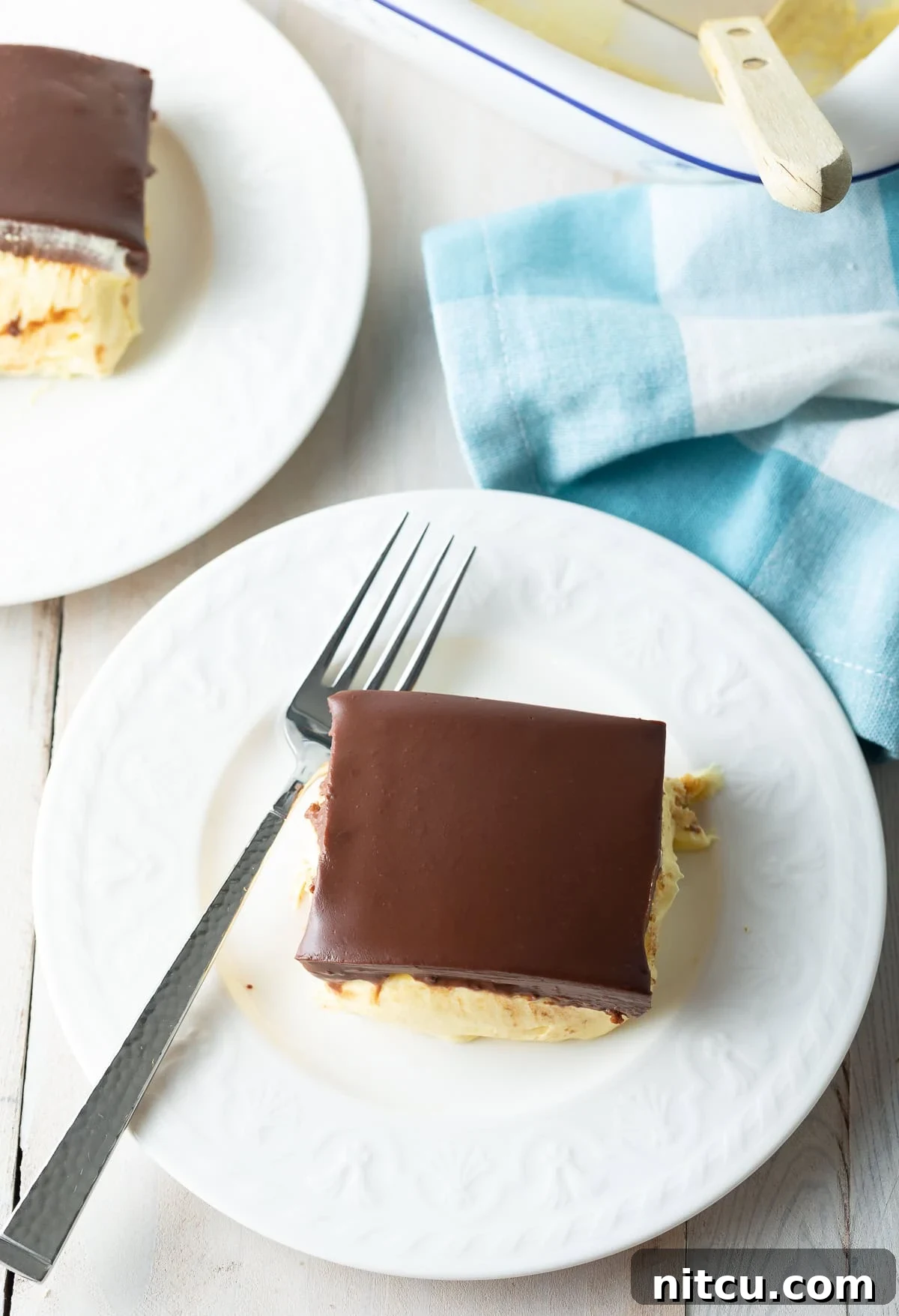 Decadent Chocolate Ganache Eclair Cake 3 An overhead shot of an entire no-bake eclair cake with chocolate ganache, sliced and ready to serve on plates with elegant blue napkins, set on a rustic wooden table, highlighting its rich, inviting presentation.